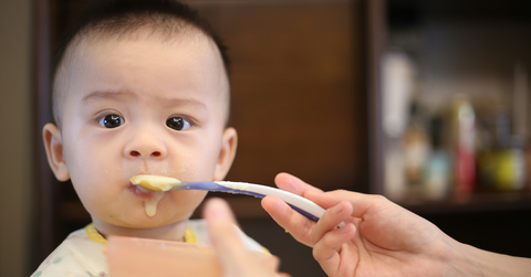A small baby is fed baby food using a spoon