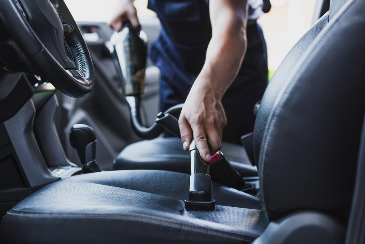 A car maintenance professional vacuums the driver seat of a car.