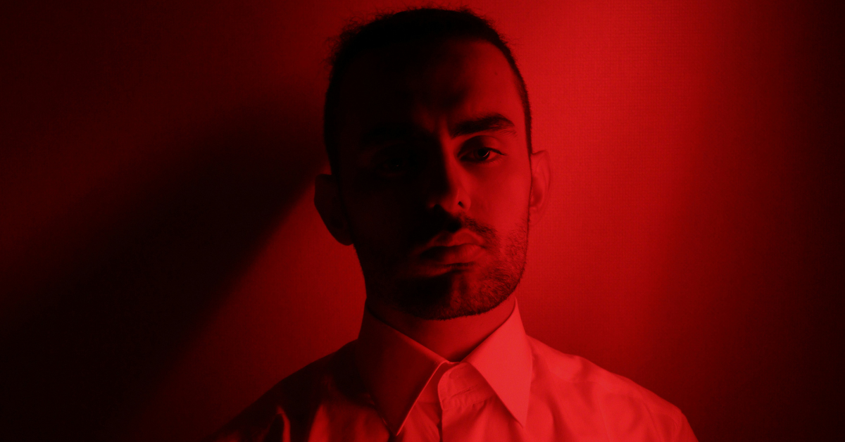 A man stands partially in the shadows as a red light shines on him