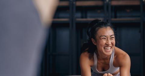 A women stretches her leg on the ground and smiles while wearing a sports bra and leggings.