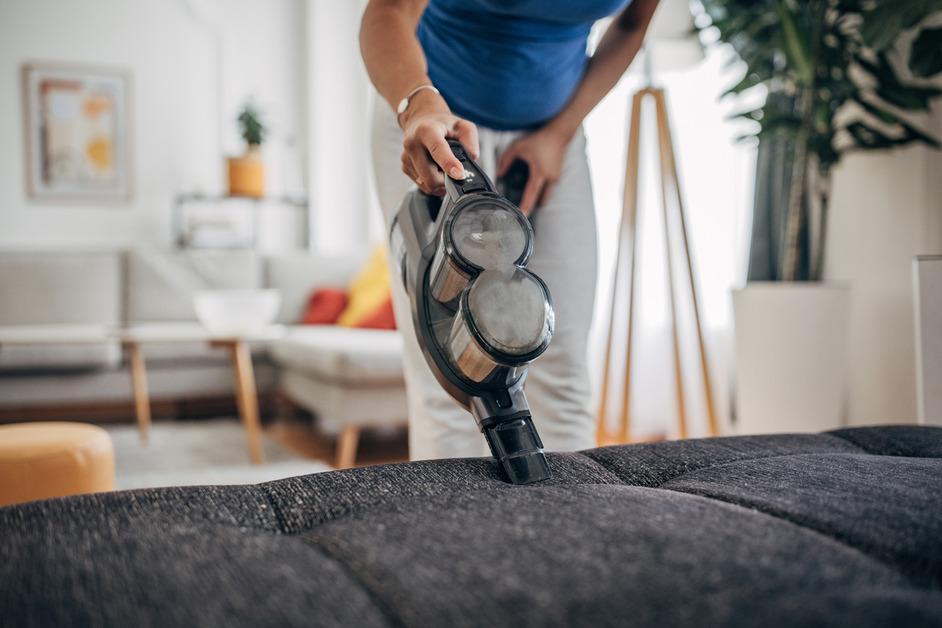 A person uses a handheld vacuum on a couch. 