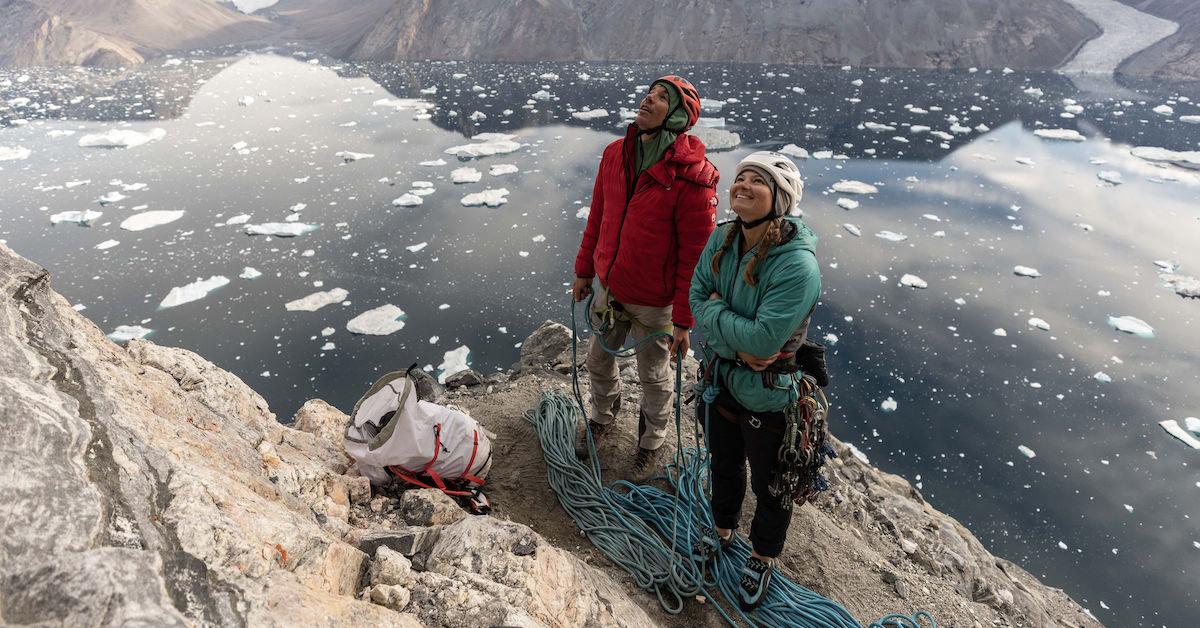 Alex Honnold and Hazel Findlay wear climbing gear and hold a bundle of ropes on the sea cliff Ingmikortilaq.