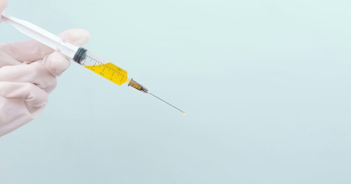 A gloved hand holds a syringe of yellow liquid 