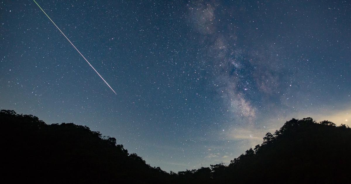 Meteor shower over a forest at night.