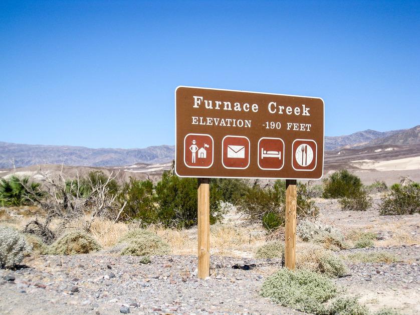 A sign in Death Valley that reads "Furnace Creek, Elevation 190 Feet" with several icons below. 