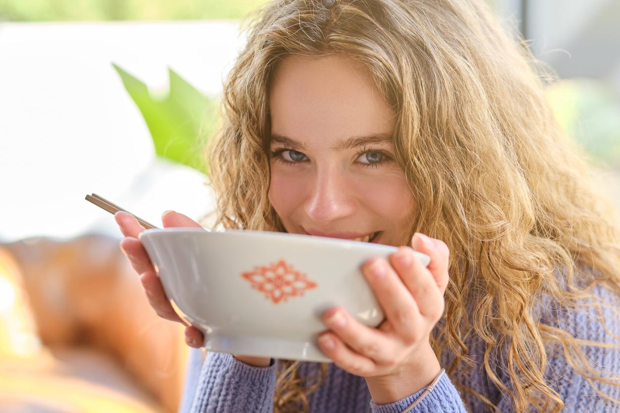 A smiling woman holds a bowl of soup to her face before consuming the soup.