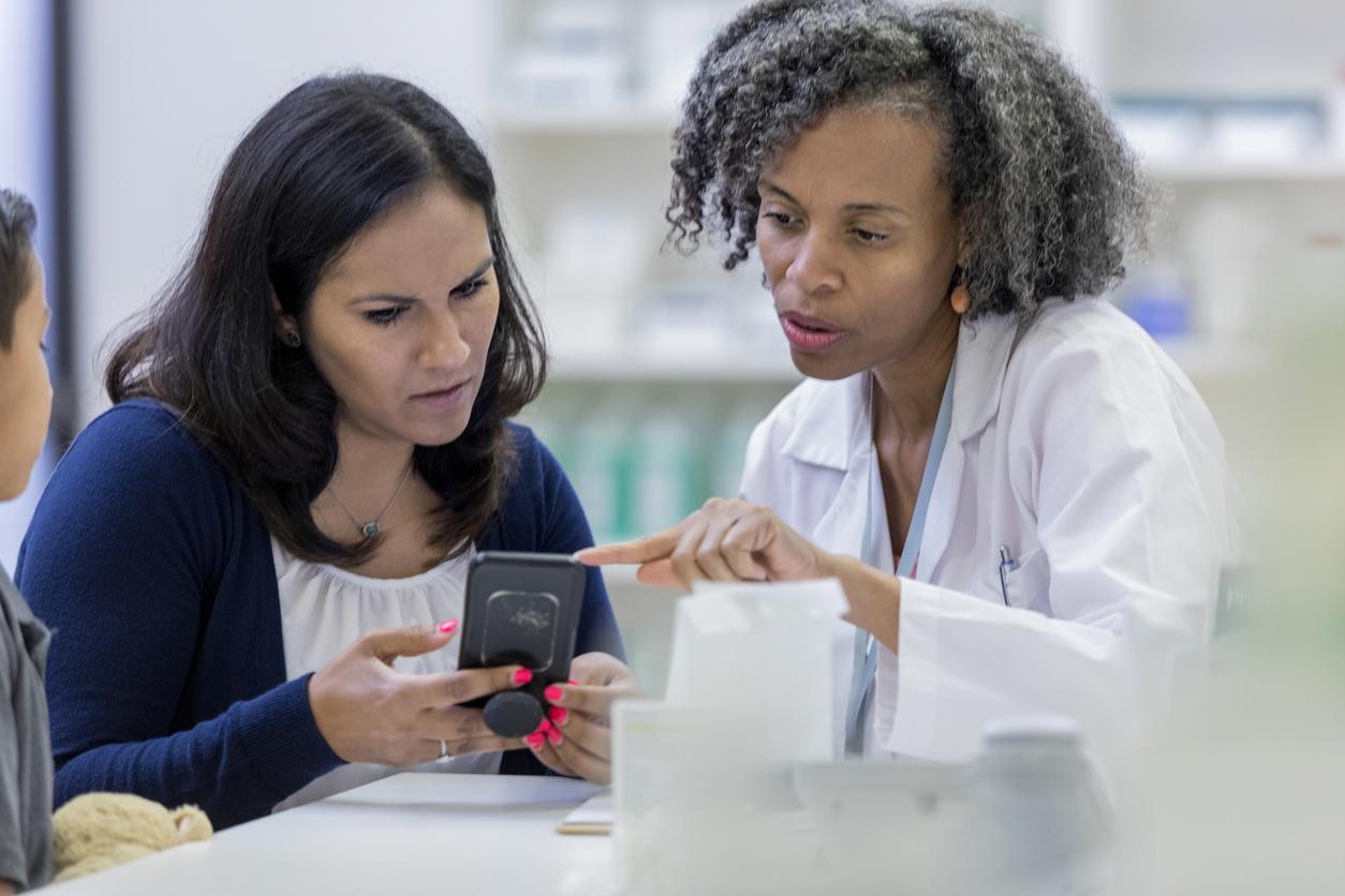 A pharmacist explains to a customer while pointing to the information on the customer's phone.