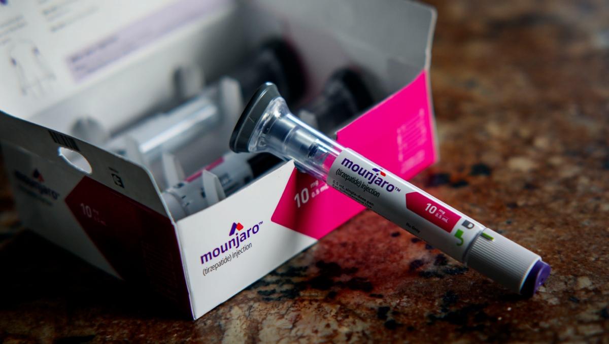 A syringe of Mounjaro medication sits on the counter resting on the box.