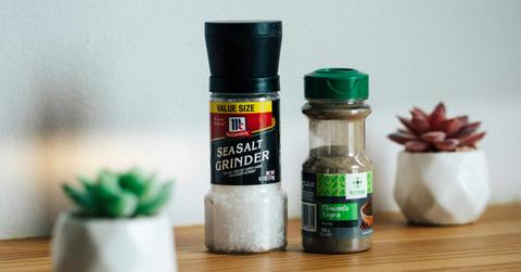 A picture of a sea salt grinder next to a black pepper container and two succulents.