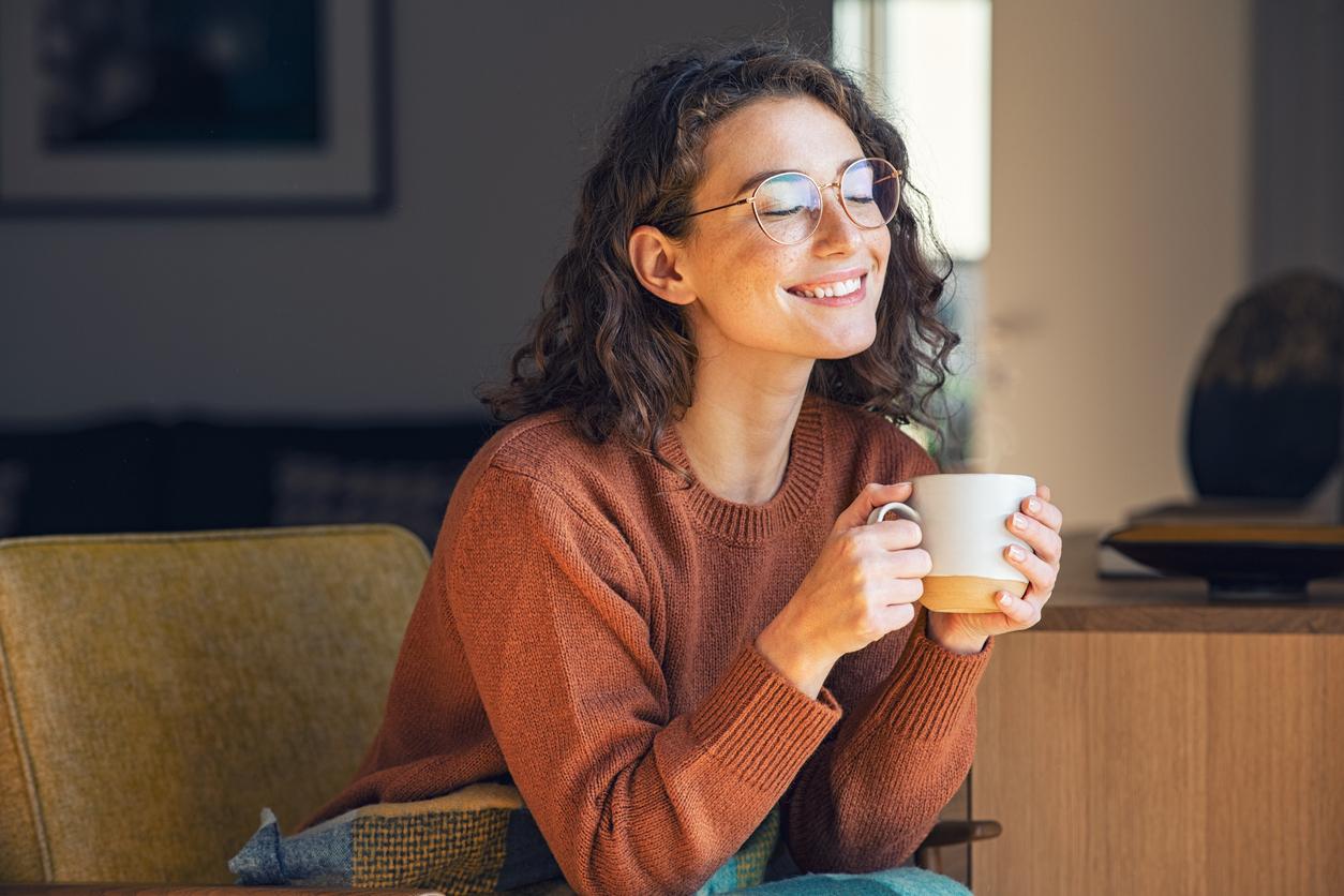 A smiling woman sips lemon gunpowder tea on her chair in her living room.