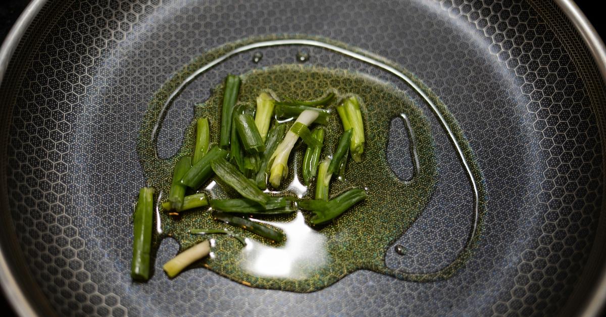 Green onions being fried in a pan with vegetable oil. 