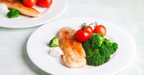Swai fish on a plate with broccoli and tomatoes.