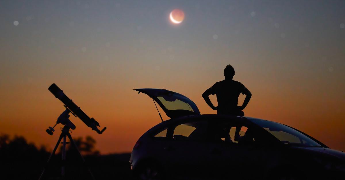 A person sitting in the car using a telescope to look at a solar eclipse. 