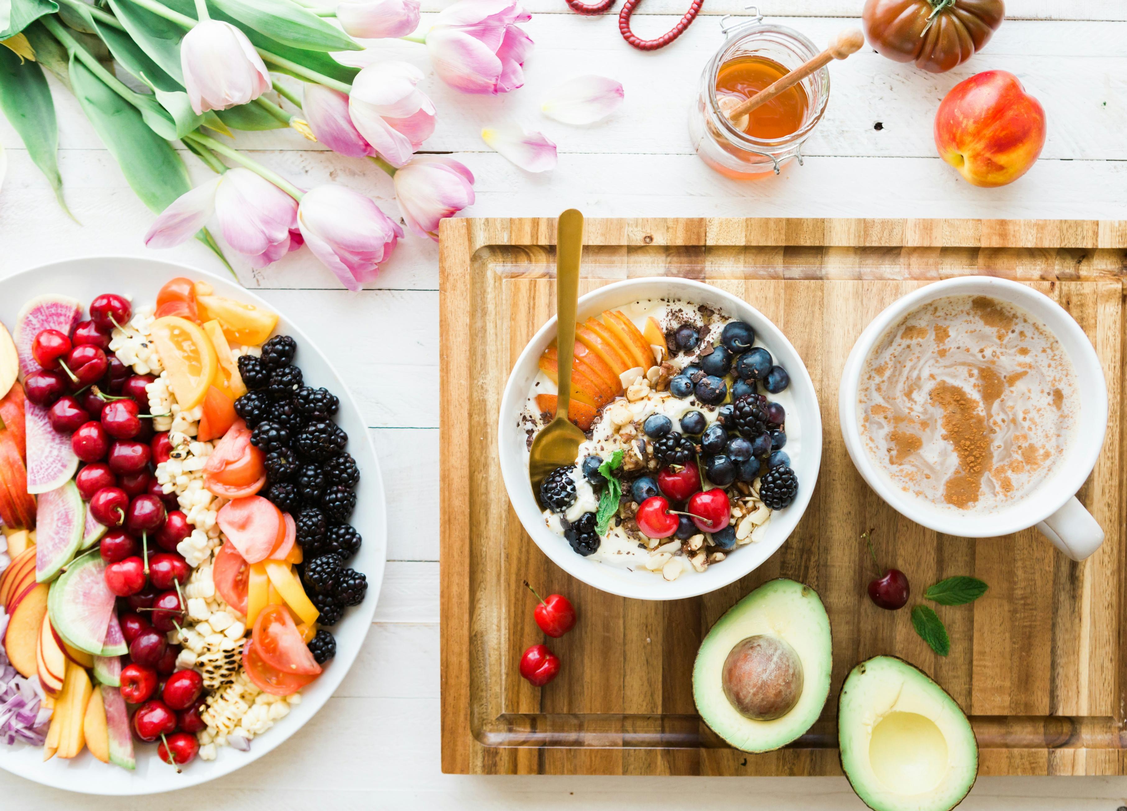 A bowl of fruit sits beside a bowl of oatmeal and a cup of coffee on top of a wooden cutting board.