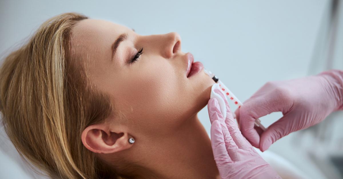 Side view of blond woman receiving a lip filler injection from two gloved hands