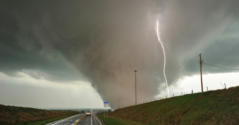 A funnel cloud heads towards the road as a bolt of lightning crashes down