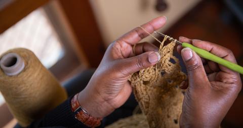Person crocheting with a small, light green hook and tan yarn.