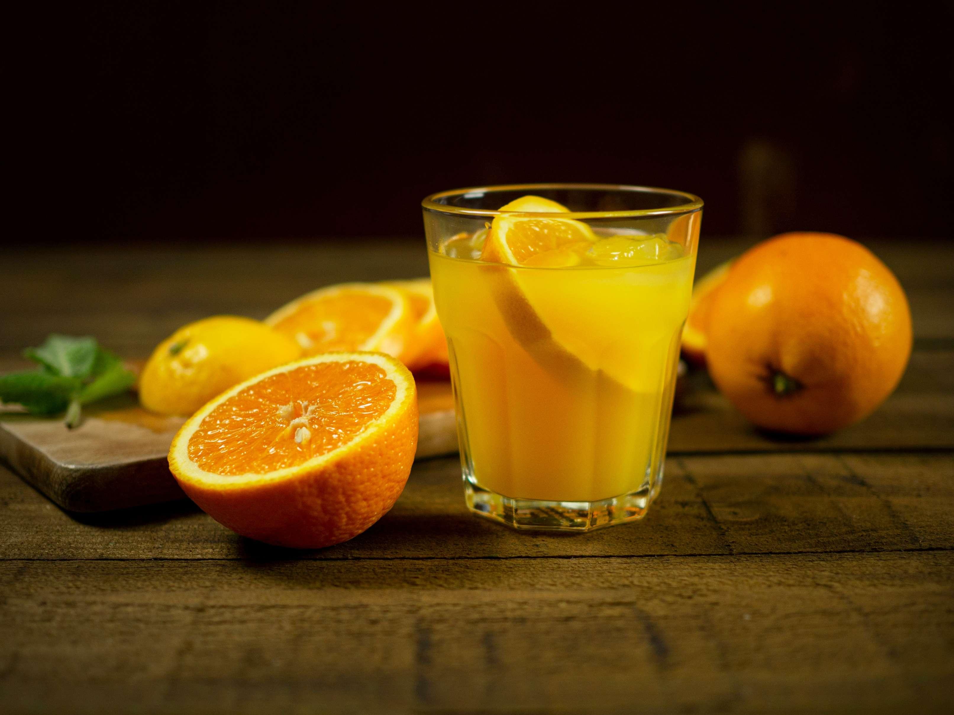 A glass of orange juice is pictured beside sliced oranges.