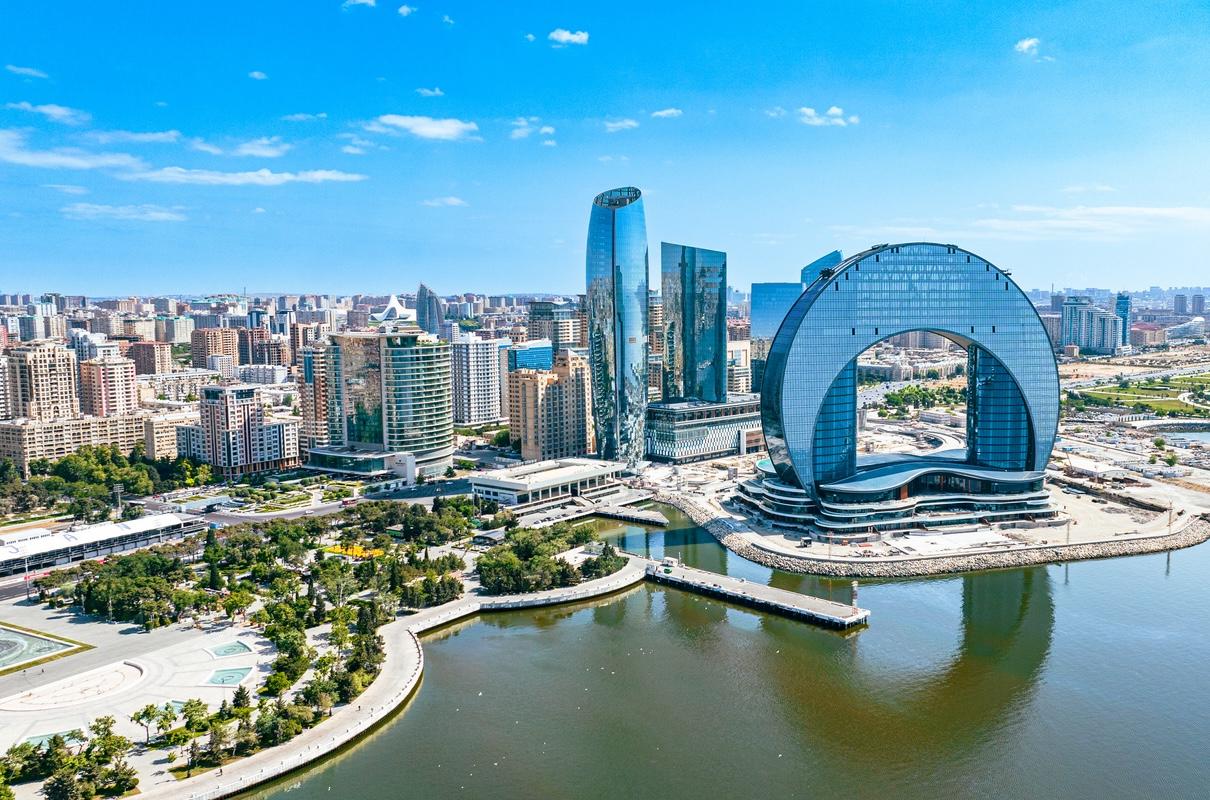 The skyline of Baku, Azerbaijan surrounded by many tall buildings and a body of water on a cloudy day.