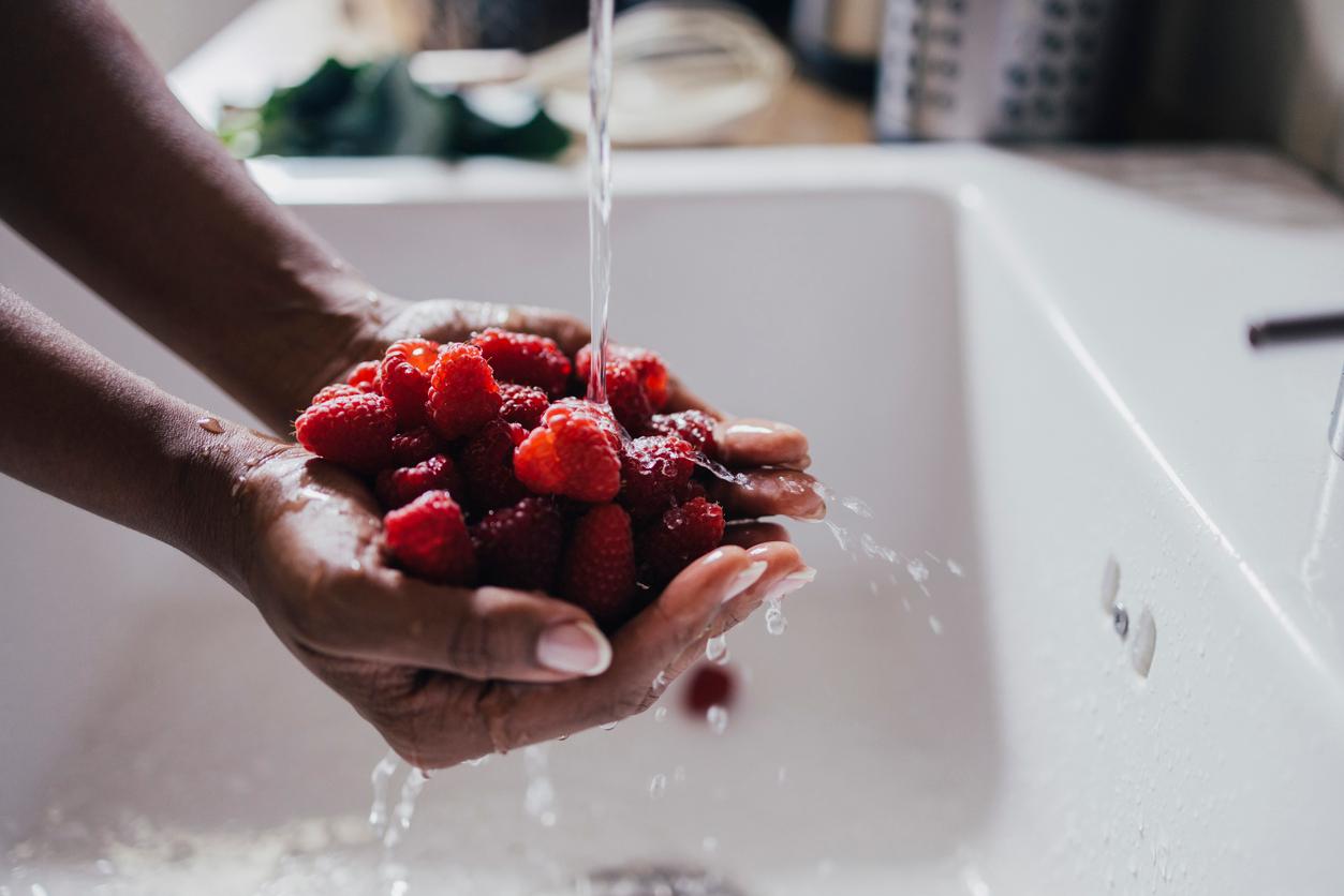 Close up of someone holding a handful of raspberries under a stream of water in the sink.