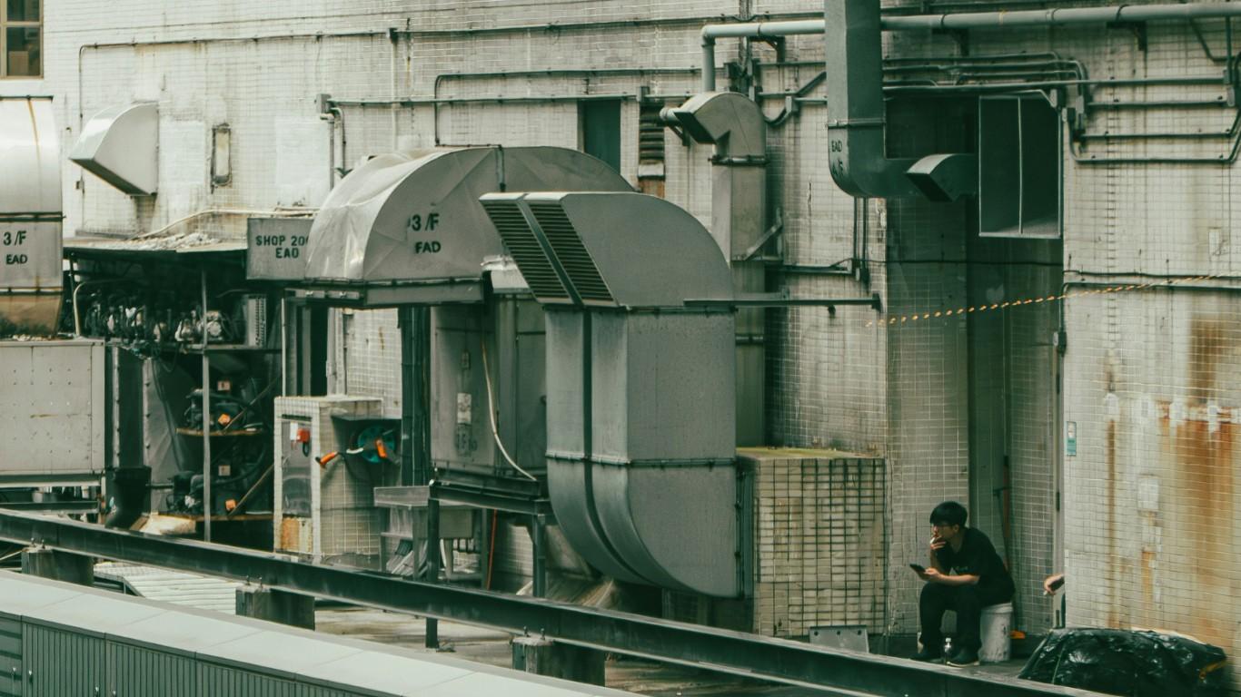 A man take a break on a city roof, sitting next to a commercial HVAC system