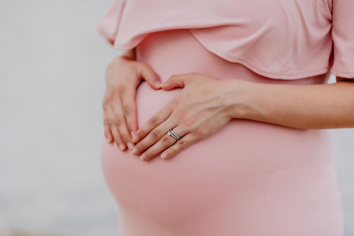 Woman forms a heart over pregnant belly in pink dress