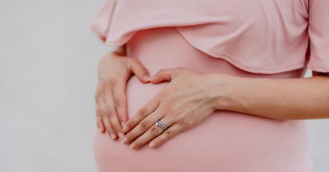 Woman forms a heart over pregnant belly in pink dress