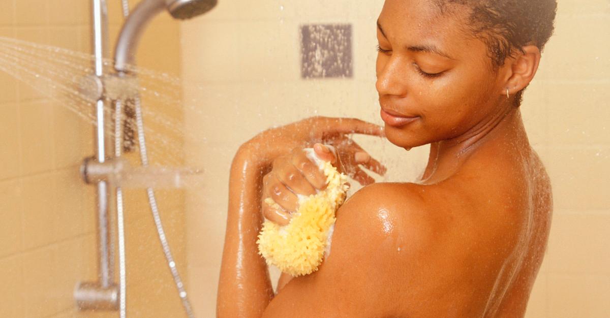 Woman cleans her shoulder with a loofa in the shower.