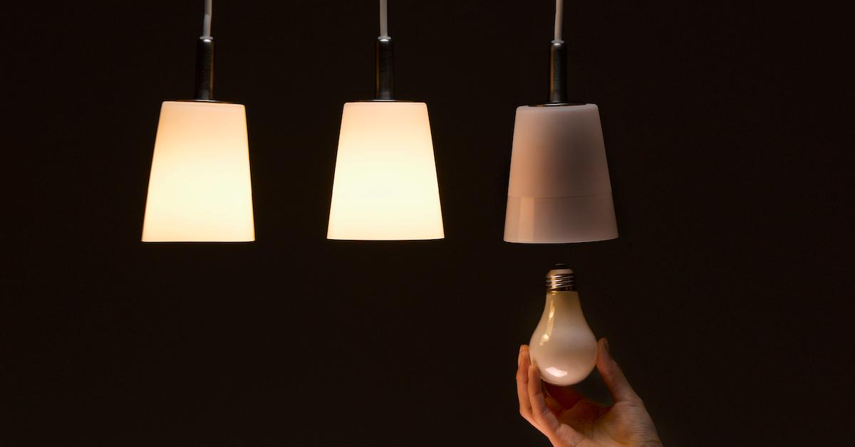 A hand places a light bulb into one of three hanging lamps