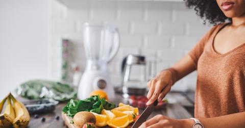 A woman prepares various vegetables on a cutting board in her kitchen.