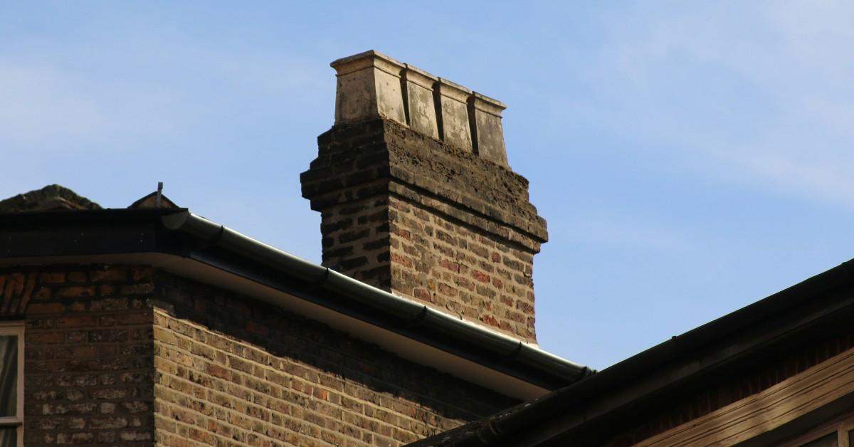 A chimney sits against a bright blue sky atop a brick house
