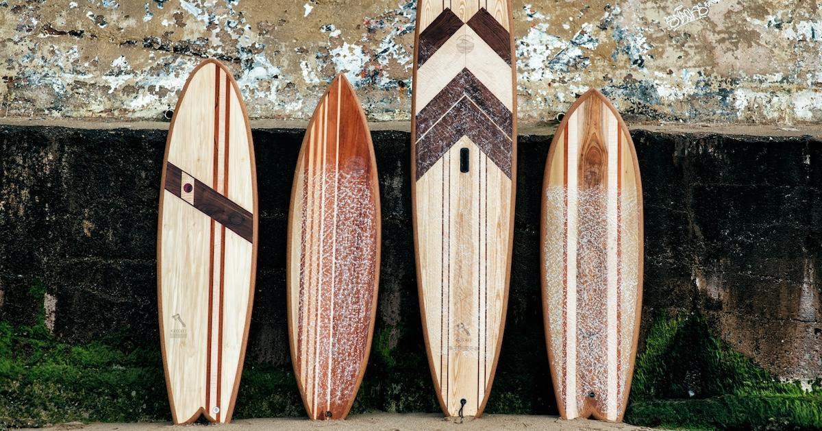 Four wooden Timber Surf Co surfboards lean against a wall outside