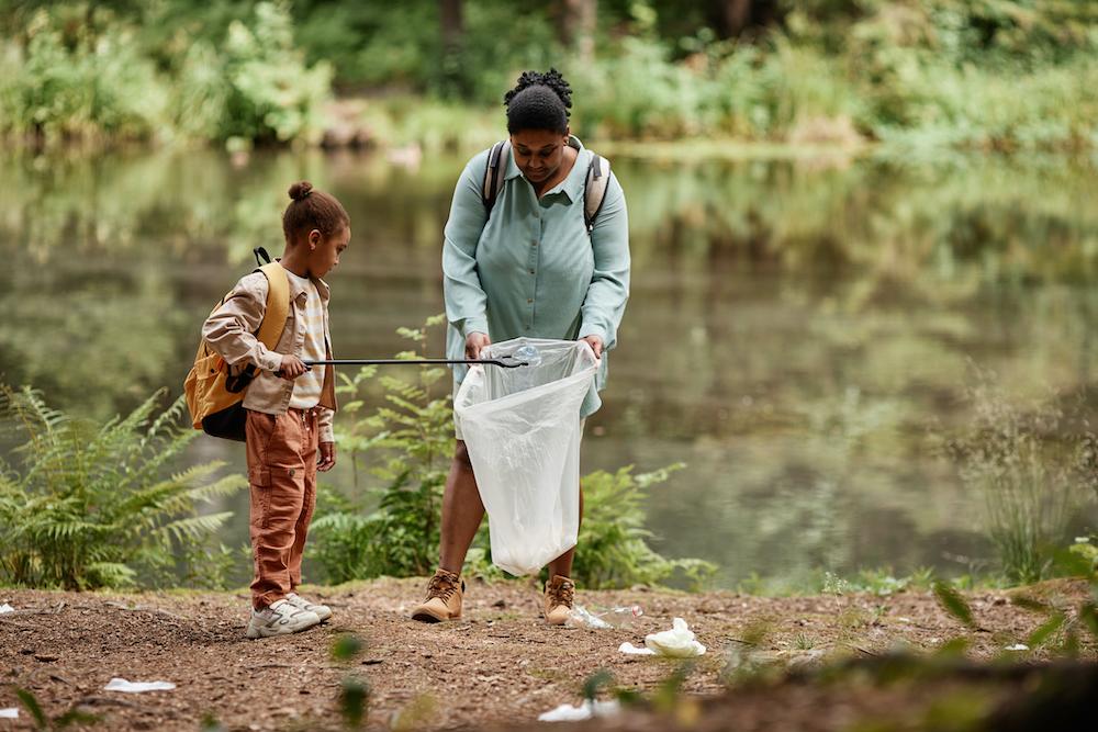 Una madre y su hijo en el bosque usando el recolector de basura para poner la basura en una bolsa de plástico.