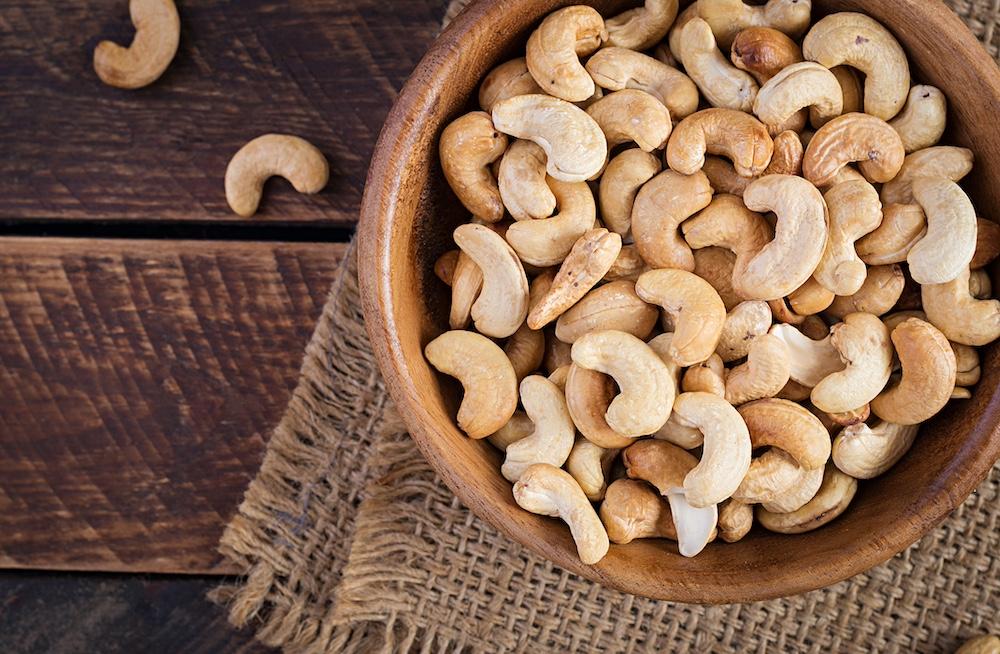 Cashews on a wooden bowl sitting on a table. 