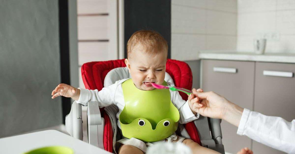Portrait of an unhappy baby in green bib crying and refusing to eat. (Representative Cover Image Source: Freepik | Cookie_studio)