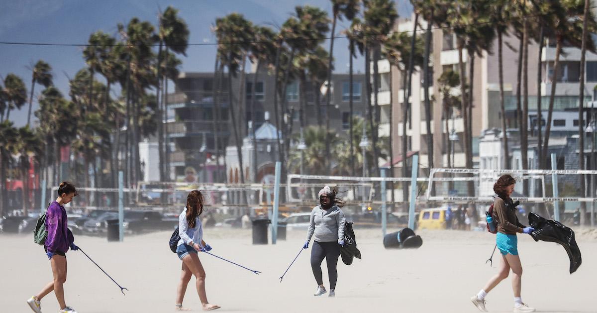 Four people carry trash pickers and garbage bags on a beach, as part of a beach cleanup.