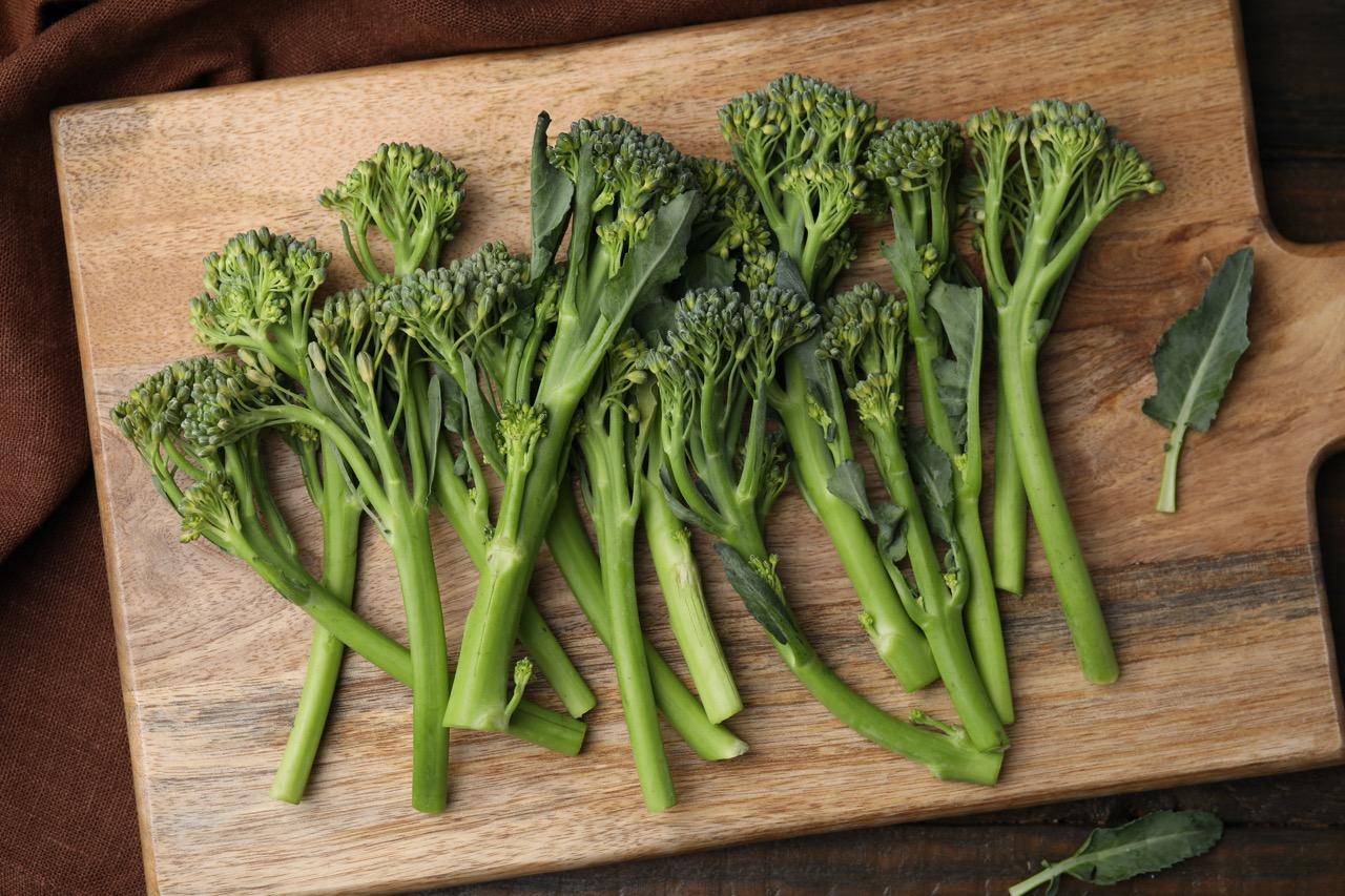 Uncooked broccoletti spread out on a wood cutting board.