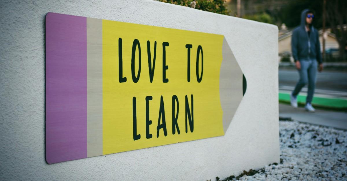 A sign says "love to learn" on a pencil outside of a school