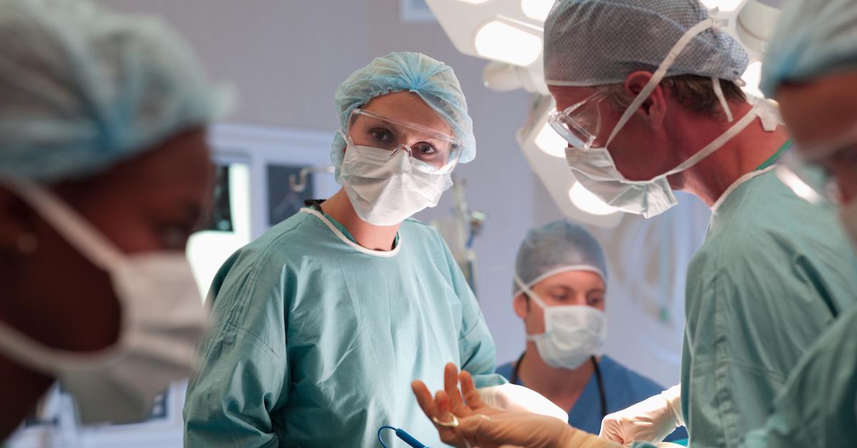 Several doctors in masks, scrubs, and hairnets working together.