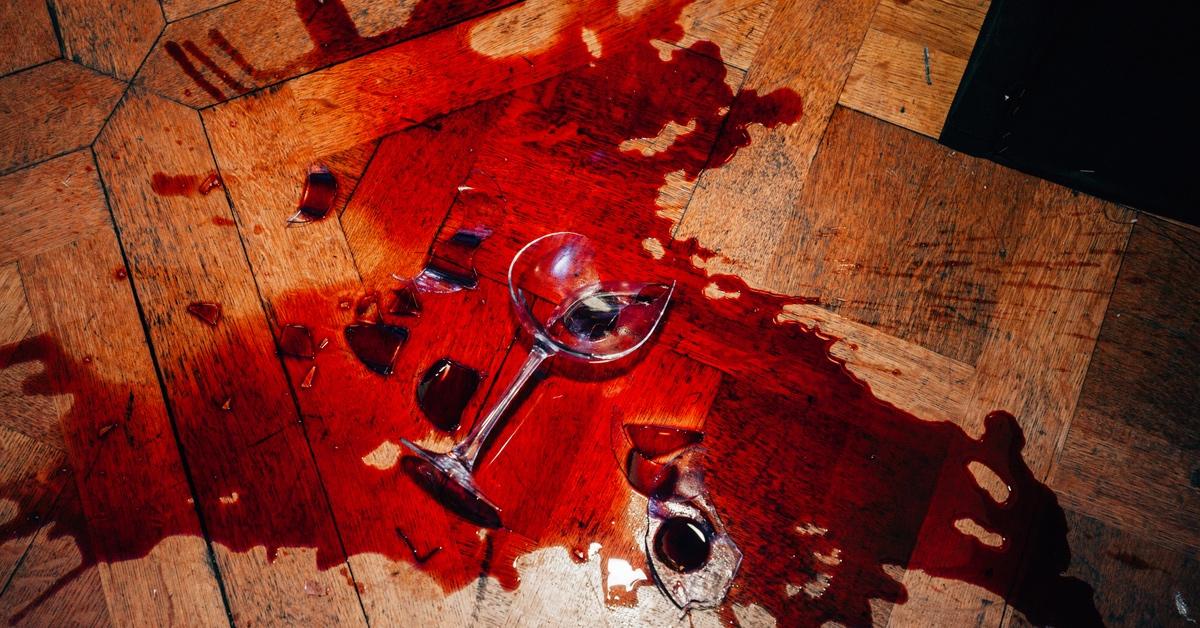 Wine glass with red wine shattered against a wood floor.