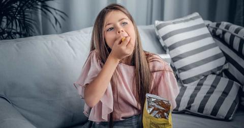 Teenage girl eating cheetos sitting on the sofa in her home. (Representative Cover Image Source: Freepik | FXquadro)