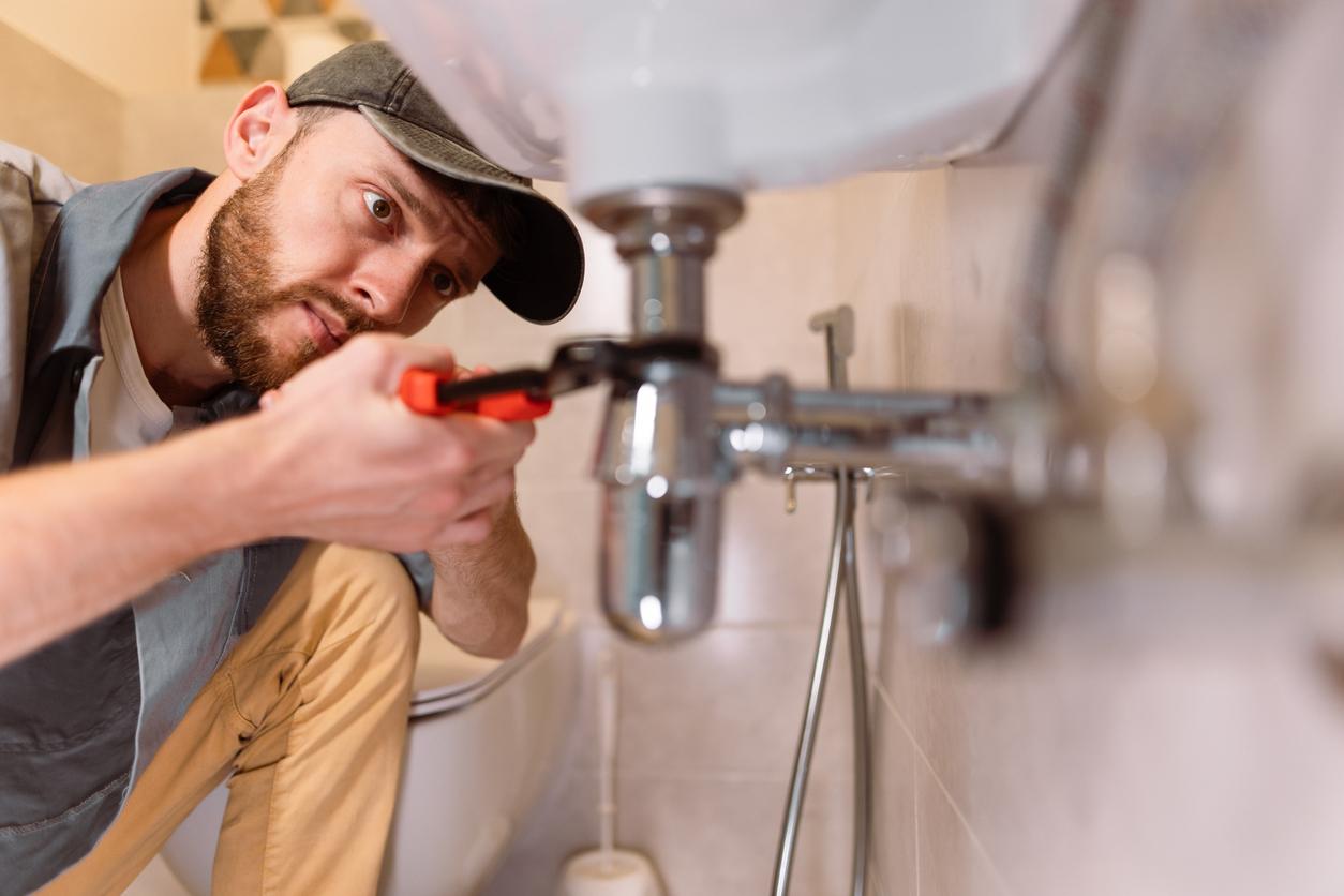 A plumber inspects the drains beneath a customer's sink in their bathroom.