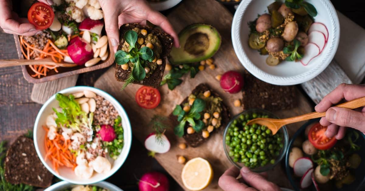 Top view of hands helping themselves to a variety of plant based side dishes