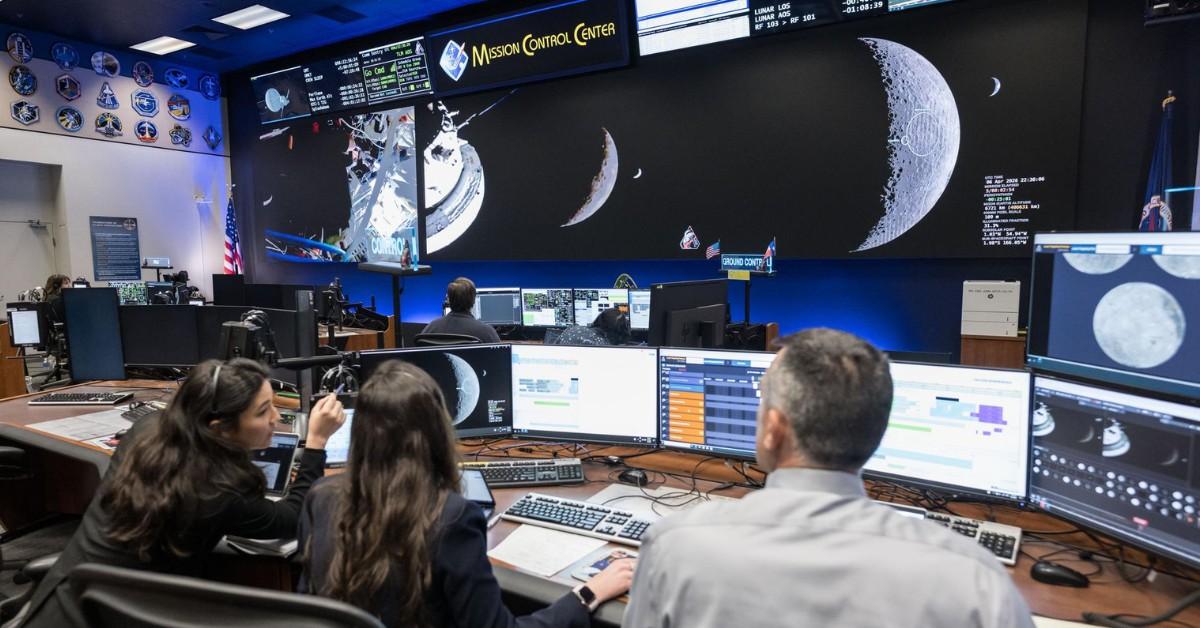 Three people sit at desks in NASA's mission control headquarters 