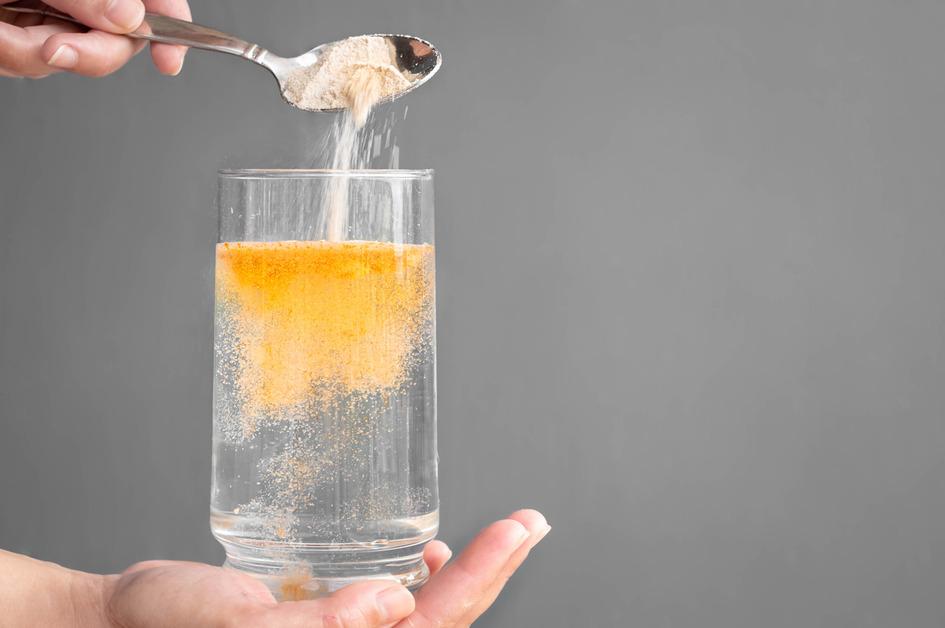 A person pours an orange powder supplement into a glass of water. 