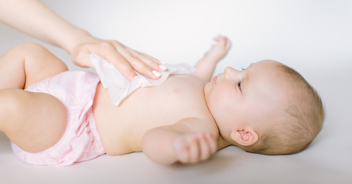 A baby lays on its back while someone uses a baby wipe