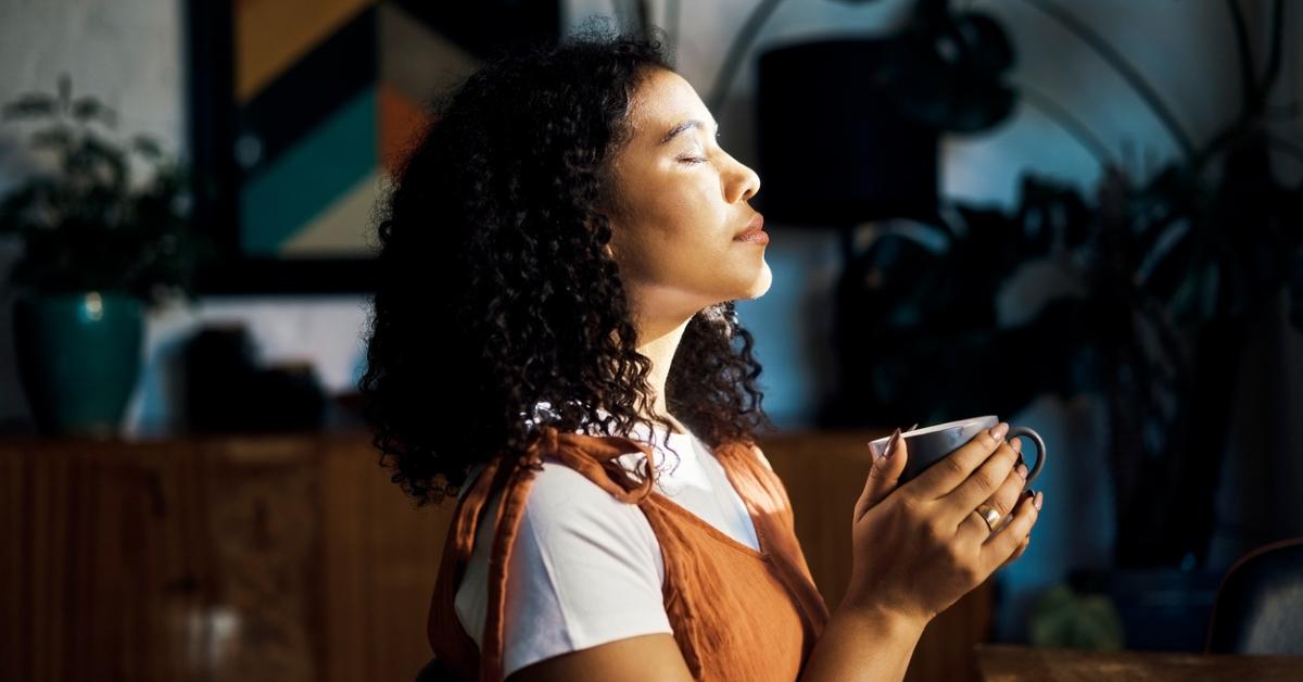 Woman closing eyes holds mug in front of window in peaceful moment