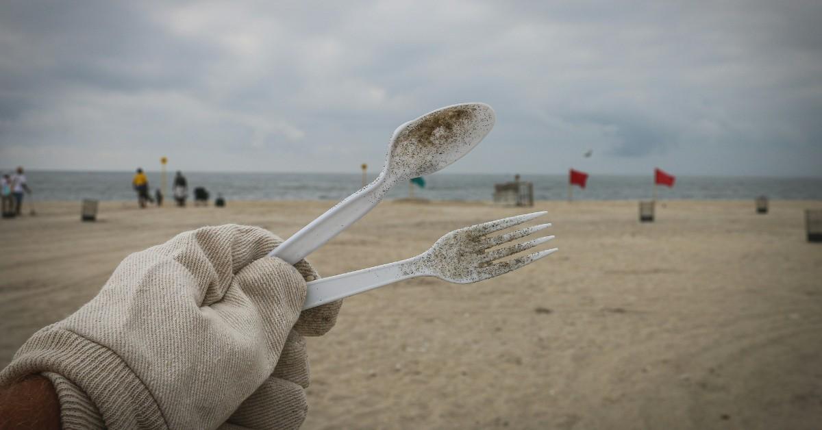 A gloved hand holds up a plastic spoon and fork that were found buried in the sand at the beach