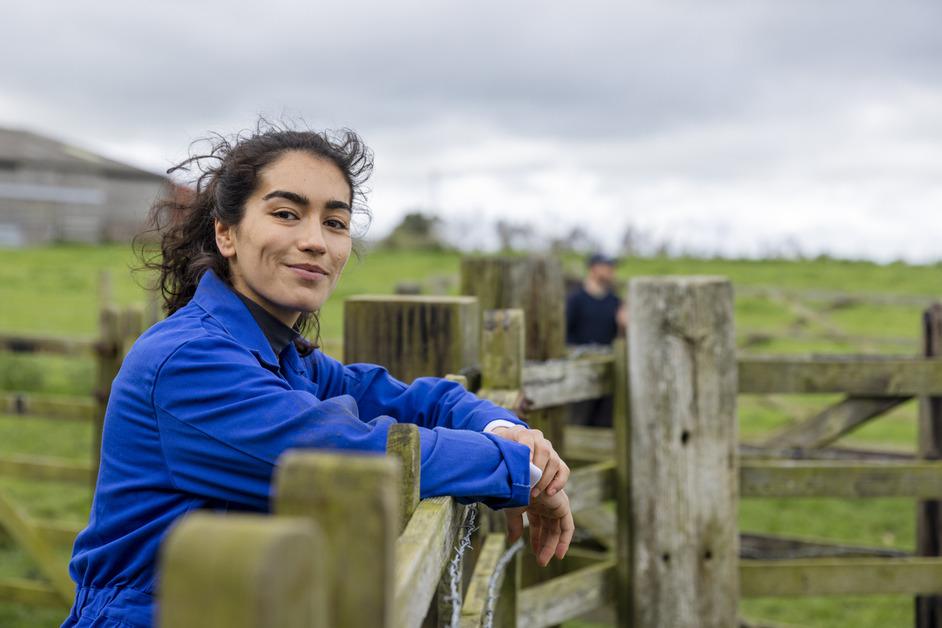 A woman wearing a blue outfit stands outside at a fence. 