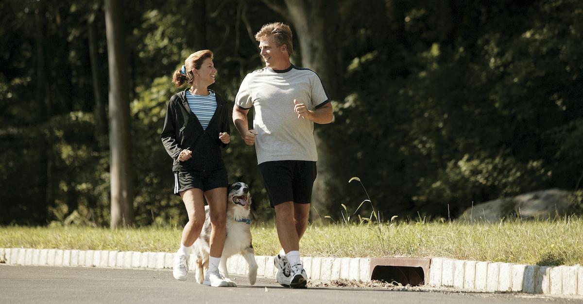 Two people jogging with their Australian Shepherd dog.